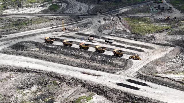 An aerial view of rigid dump trucks and excavators parked in a row at a coal mine