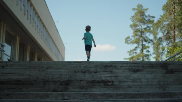Young boy running up a concrete staircase. Active child climbing tall steps outside a public building on a sunny day. Kid going up a staircase outside.