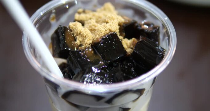 Close up of black grass jelly in fresh milk topped with brown sugar