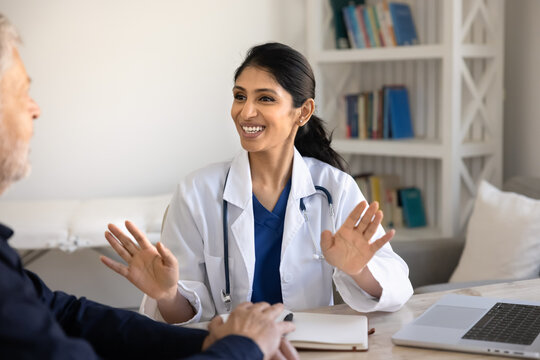 Smiling South Asian woman doctor explaining treatment to man during consultation, discussing diagnosis, answers questions, guiding patient through care plan at hospital visit. Healthcare services