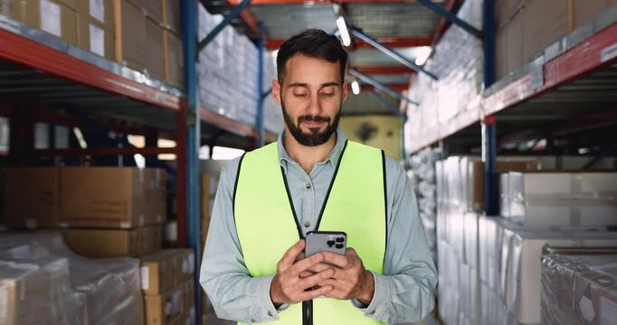 Warehouse manager man using logistic app on smartphone for inventory control, storage management, typing on cellphone at metal shelves with stacked boxes of products, smiling