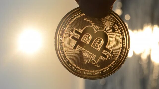 Bitcoin coin. Person holding Bitcoin coin in hand on background sea, blue sky and shining sun at dawn and sunset. Concept cryptocurrency money cryptography cryptocurrencies bitcoins. Vertical