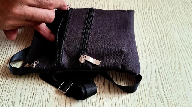 Opening zipper on small dark fabric pouch indoors, showing accessory detail, compartments, texture, and everyday use for storage, fashion, travel, and personal organization