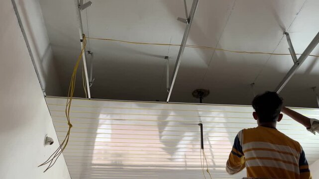 Worker standing on a platform installing a slatted false ceiling inside a room