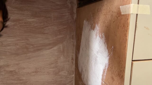 Person painting a wooden surface with white primer using a brush