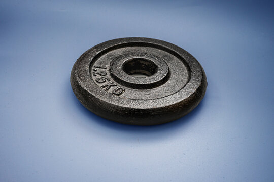 Heavy weight plate placed on a simple blue background showing a round design and weight marking