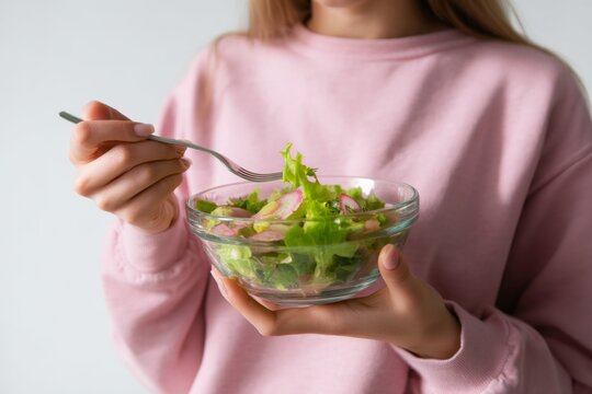 Healthy salad being enjoyed by a woman in a stylish pink sweater. A colorful bowl filled with fresh greens showcasing vibrant ingredients. Generative AI