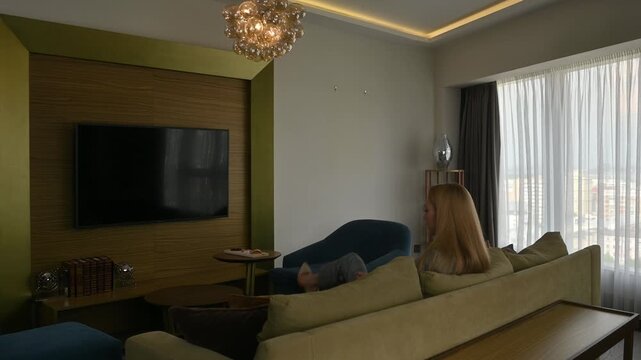 Businesswoman in a formal suit arriving at her luxury hotel suite, putting her luggage aside and resting on the comfortable sofa after a long and tiring business trip