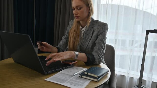 Young woman entering credit card details on a laptop to make an online purchase or book a service while sitting at a desk in her hotel room during a business trip