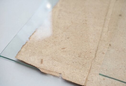 A stack of textured handmade recycled paper sheets placed underneath a transparent pane of glass