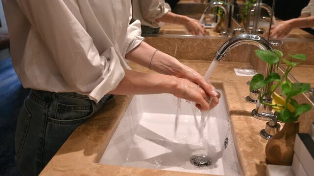 Person meticulously washing their hands under running water from a modern faucet in a clean, well-lit bathroom, promoting hygiene and personal care