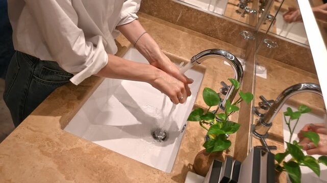 Young woman meticulously washing her hands with running water from a chrome tap in a stylish bathroom, demonstrating proper personal hygiene and cleanliness to prevent virus spread