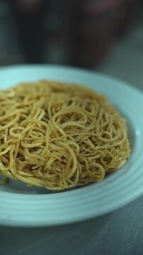 Vertical video close up of crispy fried golden noodle nest served on white plate in kitchen
