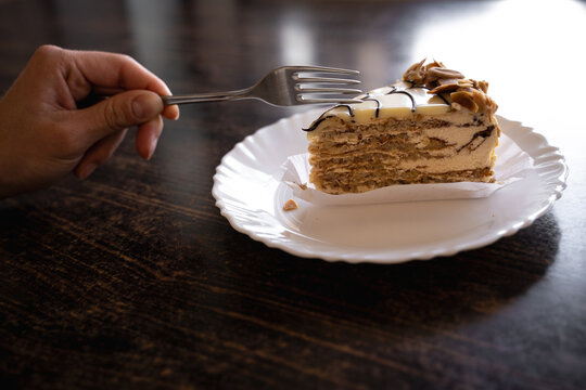 Close-up of a woman enjoying a slice of traditional Esterh&aacute;zy cake with a fork at a cafe table. Dessert, dining and European cafe lifestyle concept.