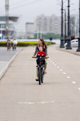 Fototapeta premium Mother cycling with young son seated in front along urban pathway with soft city background