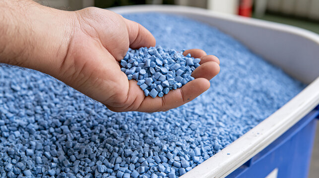 Close-up of a worker holding a handful of small blue plastic pellets resin granules in an industrial manufacturing factory setting for polymer production and recycling