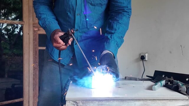 Professional metalworker welding steel while wearing a protective welding helmet, gloves and safety clothing in a workshop environment.