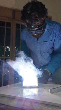 Professional metalworker welding steel while wearing a protective welding helmet, gloves and safety clothing in a workshop environment.