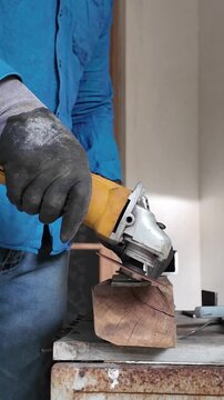 Metal fabrication worker operating a handheld angle grinder indoors to cut a steel component, demonstrating industrial workshop craftsmanship.
