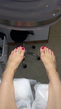Vertical video of female feet with red polish in a beauty salon before a pedicure procedure. Feet of a client under dust collector lamp in podology room prepared for foot care and cosmetic treatment.