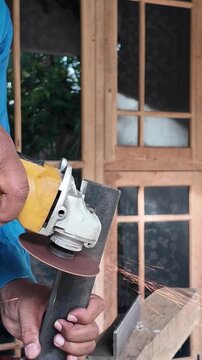 : Detailed close-up of a handheld angle grinder being used on a steel metal component, showing industrial fabrication and metalworking in action.

