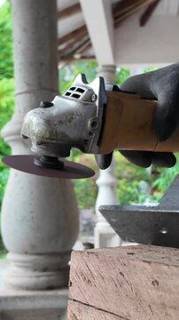 Metalworker grinding and shaping a steel component with a handheld angle grinder during fabrication work in an outdoor workshop.