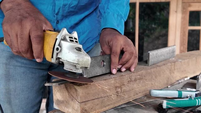Skilled worker using a handheld angle grinder to cut a steel metal piece in a workshop, with sparks generated during the cutting process