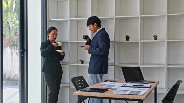 Asian business colleagues taking coffee break together near office window for corporate informal meeting, relaxing teamwork discussion, workplace communication and partnership concept