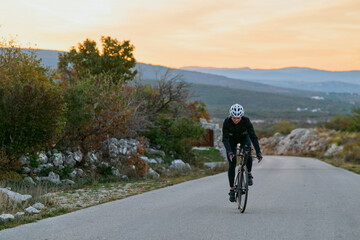 Fototapeta premium Road Cyclist Training Through Scenic Rural Hills at Sunset on a Quiet Asphalt Road