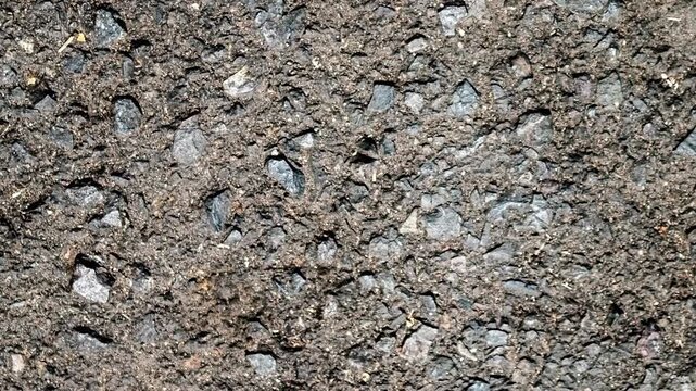 Seamless rotating loop of a dark asphalt road surface texture, featuring rough crushed stone aggregates and dark tar pavement.