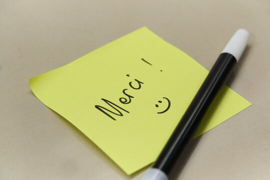 Handwritten Merci Thank You text in French on yellow sticky note with marker pen