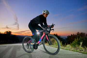 Naklejka premium Female Cyclist Training On Road Bike At Sunset With Helmet And Aero Handlebars For Fitness
