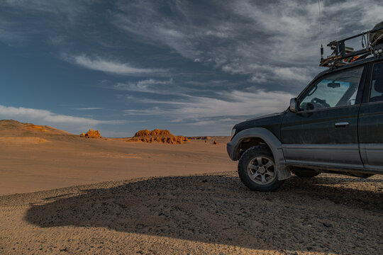 Off-road expedition suv car parked in a desert canyon with red rock formations under a dramatic cloudy sky, remote travel and adventure concept