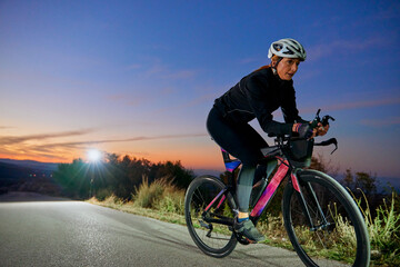 Naklejka premium Female Cyclist Training On A Road Bike At Sunset On A Rural Road