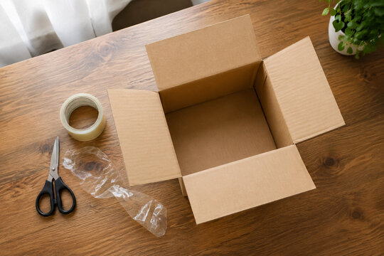 Top-down view of opened cardboard shipping box with tape and scissors.