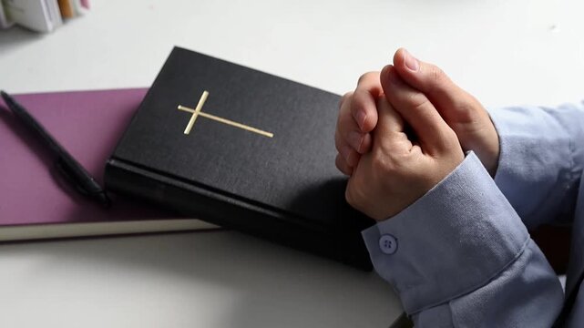Hands Clasped in Prayer Beside Bible and Open Notebook