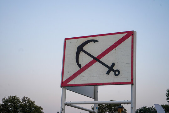 Close-up low angle view of white square maritime sign with red border and crossed out anchor symbol against clear dusk sky background.