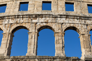 Obraz premium Ancient Arches of Pula Arena Roman Amphitheater in Croatia. Close view of ancient stone arches and weathered masonry of Pula Arena in Croatia against a clear blue sky.