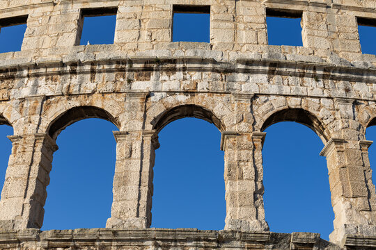 Ancient Arches of Pula Arena Roman Amphitheater in Croatia. Close view of ancient stone arches and weathered masonry of Pula Arena in Croatia against a clear blue sky.