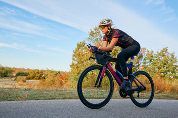 Fototapeta premium Female Cyclist Riding Aerodynamic Road Bike on Country Road During Sunny Outdoor Training Session