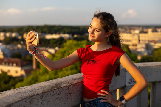 Teenage Girl Taking Smartphone Selfie at Pula Viewpoint. Teenage girl in a red top taking a smartphone selfie at a scenic viewpoint overlooking Pula in warm evening sunlight.