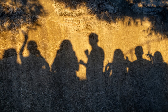 Group Shadows Cast on Textured Wall in Golden Sunlight. Shadows of a group of people cast across a weathered textured wall in warm golden sunlight.