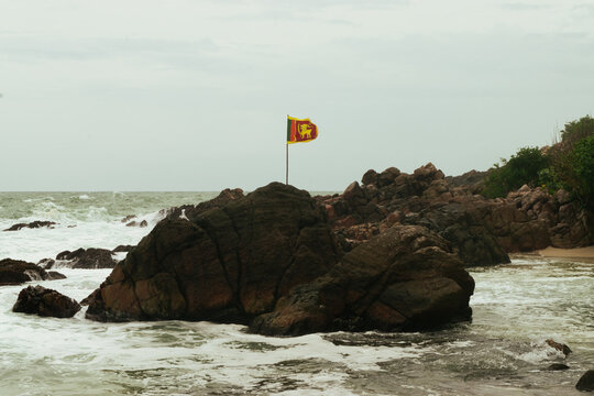 Lanka national flag waving on top of rocky coast with crashing ocean waves