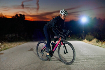 Naklejka premium Female Cyclist Riding Road Bike at Dusk With Helmet and Light for Night Training