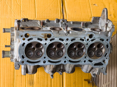 Four cylinder engine cylinder head showing combustion chambers and valves resting on cardboard.