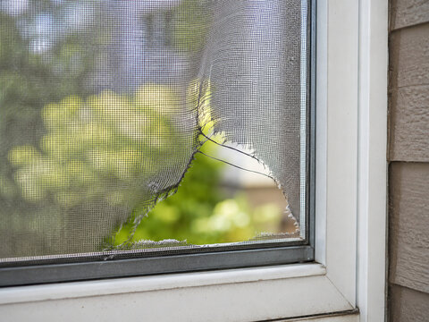 Torn window screen mesh with large hole in residential window