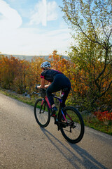 Fototapeta premium Female Cyclist Training on Quiet Country Road at Sunset in Autumn Landscape With Scenic Trees