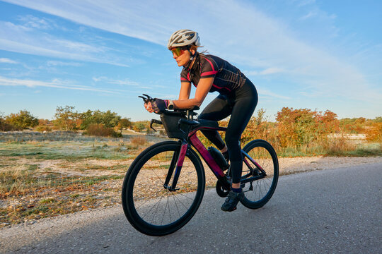 Female Cyclist Training on Road Bike at Sunrise With Aerodynamic Helmet and Sunglasses
