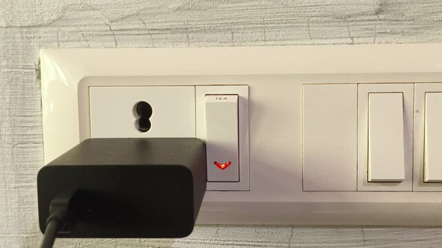 Closeup of hand connecting smartphone or laptop device charger adapter plug into indian electric power outlet or socket hole on wall and switch on. Daily charging device lifestyle concept.