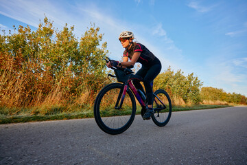 Fototapeta premium Female Cyclist Training On Road Bike Along Country Road At Sunrise